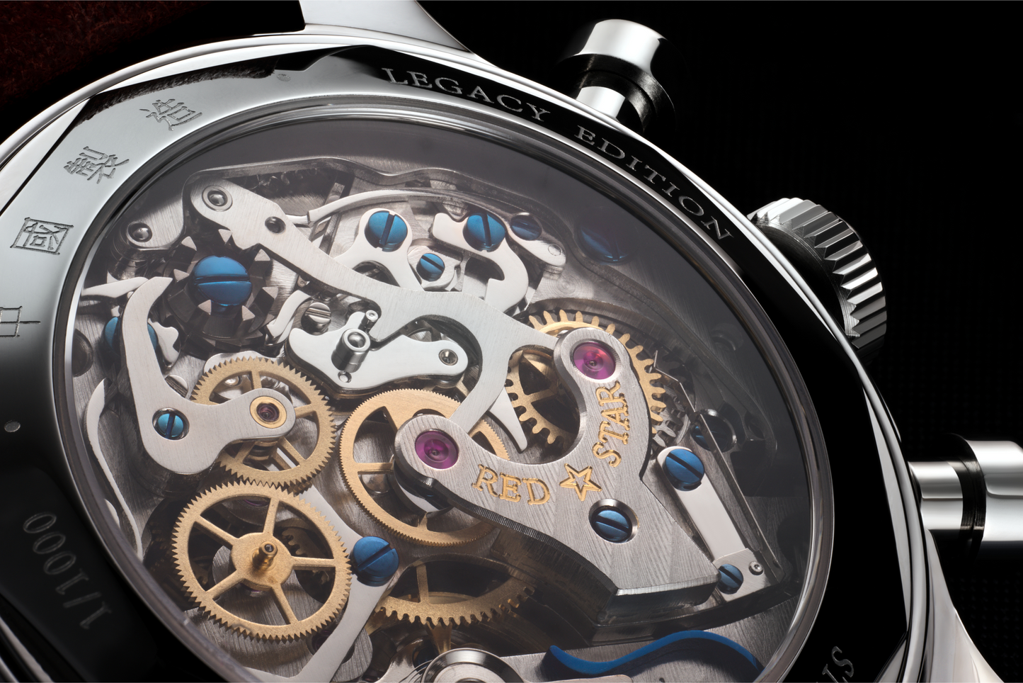 Close-up of a luxury watch movement showing intricate gold-toned gears, polished silver-toned steel components, and small blue and purple accents behind a clear dial cover.