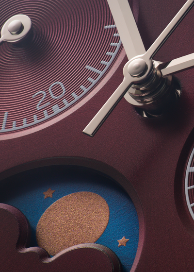 Close-up of a wristwatch dial with burgundy concentric rings, silver hands, a moon phase window with a blue sky and gold moon, and white hour markers.