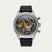 A luxury skeleton watch with a silver stainless steel case, black leather strap, and a highly visible gold and silver mechanical movement visible through the clear dial.