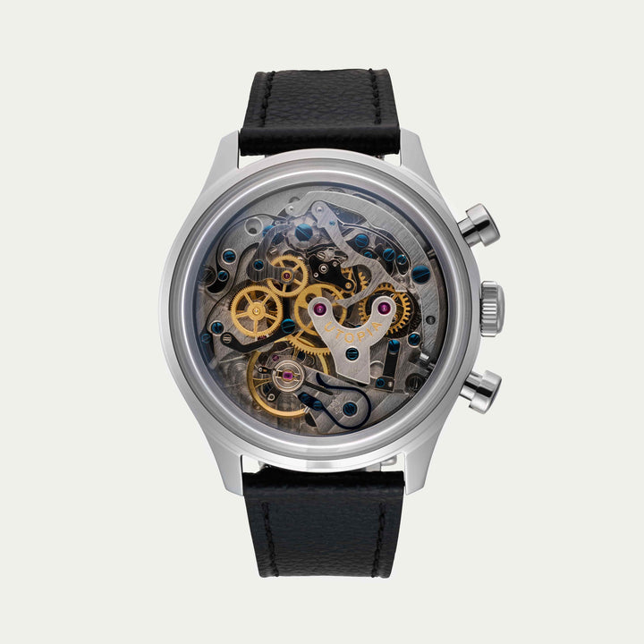 A luxury skeleton watch with a silver stainless steel case, black leather strap, and a highly visible gold and silver mechanical movement visible through the clear dial.