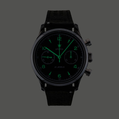 A black chronograph watch with a textured black strap, featuring glowing green hands, hour markers, and subdials on a dark gray background.
