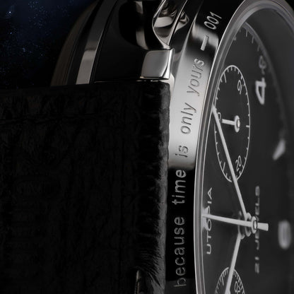 Close-up of a luxury watch featuring a black textured leather strap, a polished silver-tone stainless steel case, and a black dial with white markings and text.