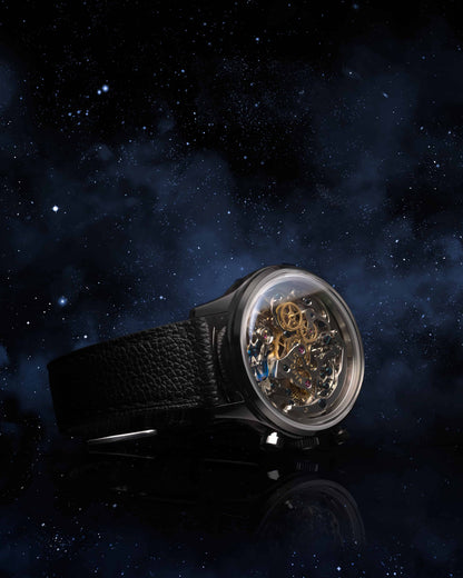 A luxury skeleton watch with a black textured leather strap and a clear crystal case revealing intricate gold-toned mechanical gears, set against a dark starry space background.